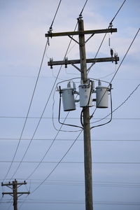 Low angle view of power lines against cloudy sky