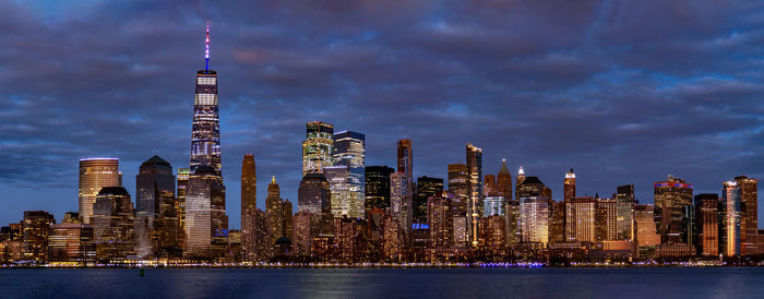 Illuminated buildings in city against cloudy sky