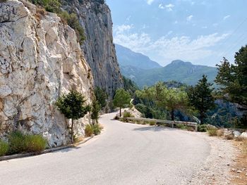 Road amidst trees and mountains against sky