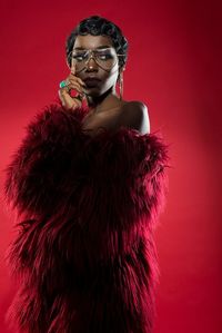 Young woman wearing eyeglasses and fur clothing standing against red background