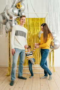 Happy family holding balloons standing against decorated wall