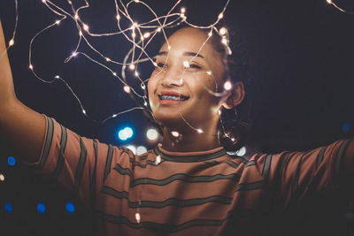 Smiling young woman holding illuminated string lights at night