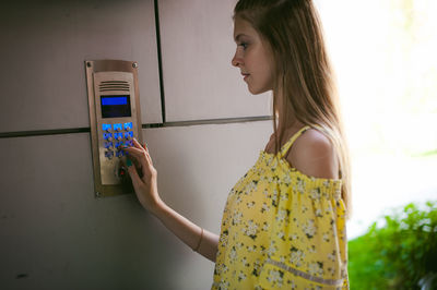 Young woman entering password on security system by door