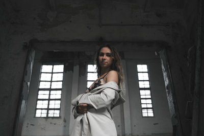 Low angle portrait of woman standing against old wall