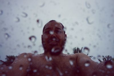 Portrait of shirtless man seen through wet glass during monsoon