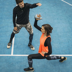 High angle view of instructor assisting woman in exercising at gym