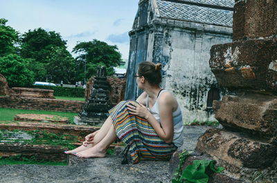 Woman looking away while sitting by built structure