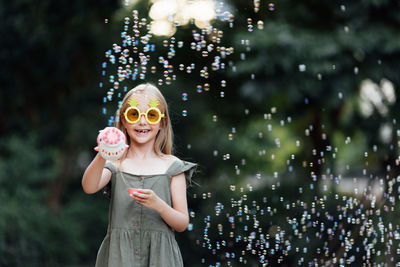 Portrait of young woman wearing sunglasses while standing against illuminated christmas