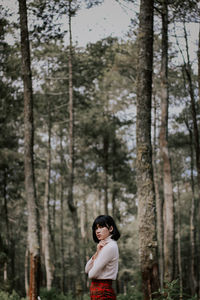 Side view of woman standing against trees in forest