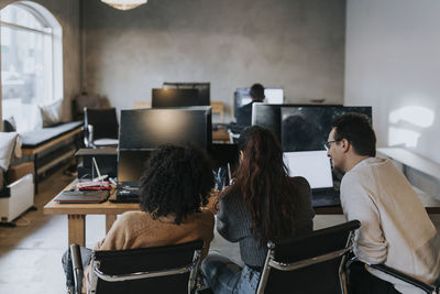 Rear view of multiracial computer programmers discussing at desk in creative office