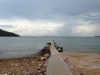 Pier leading to sea against clouds