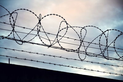 Low angle view of silhouette razor and barbed wire against sky
