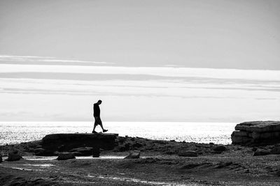 Rear view of man walking at beach against sky