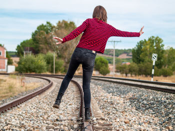 Teenage girl standing on railroad track against sky