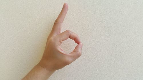 Cropped hand showing ok sign against white wall