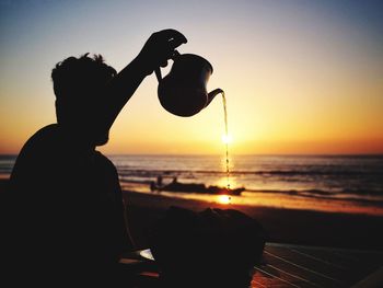 Silhouette of person photographing sunset over sea