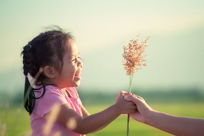 Cropped hand of mother giving flowers to happy daughter against sky