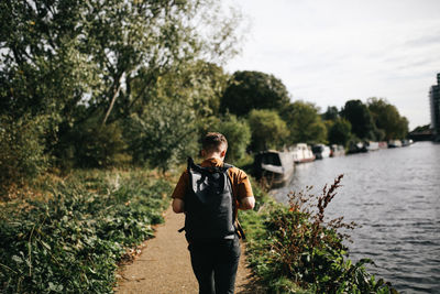 Full length rear view of man standing at riverbank against sky