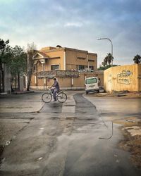 Man riding bicycle on street against buildings in city