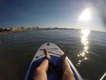 Low section of person relaxing on paddleboard in sea against sky