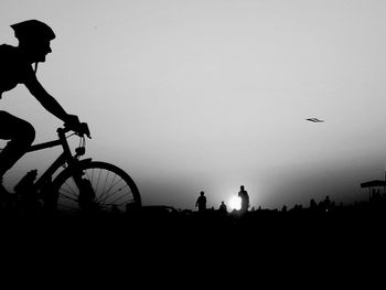 Silhouette people riding bicycle against sky during sunset