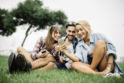 Smiling young woman with friends using phone on field