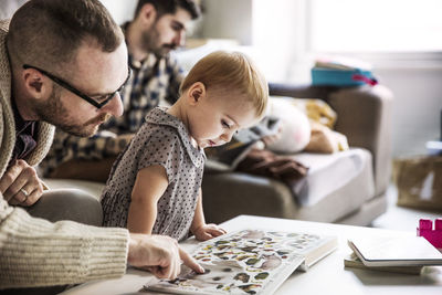 Father showing picture book to girl with partner sitting in background