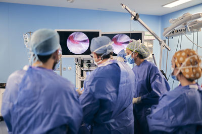 Doctors operating surgery through computer screen while standing at operation room during covid-19