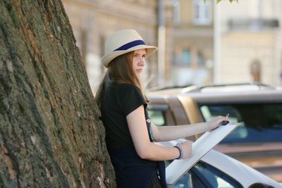 Female artist with canvas leaning on tree trunk