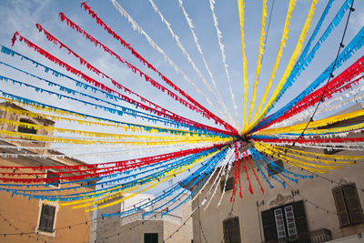 Low angle view of colorful streamers amidst buildings against sky