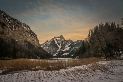 Scenic view of lake by snowcapped mountains against sky during sunset