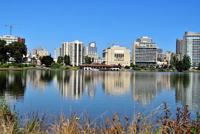 Reflection of buildings in lake against clear blue sky