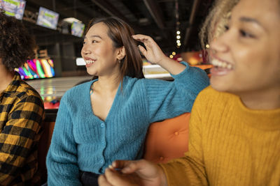 Happy young friends sitting on sofa at bowling alley