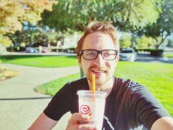 Portrait of smiling man drinking glass in park