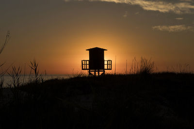 Silhouette hut on field against sky during sunset