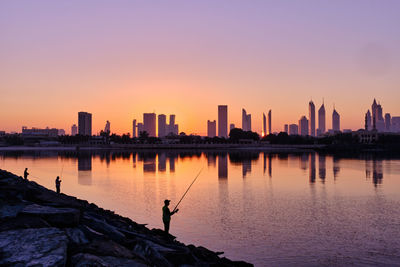 Silhouette buildings by sea against sky during sunrise