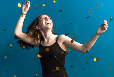 Young woman with arms raised standing against blue background