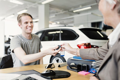 Happy man receiving car keys from saleswoman at desk in showroom