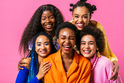 Portrait of smiling friends standing against pink background