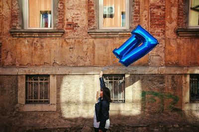 Side view of woman holding helium balloon against old building