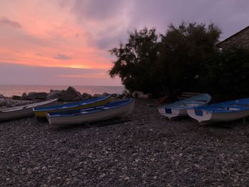 Boats moored on beach against sky during sunset