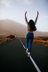 Rear view of woman jumping on road against mountain