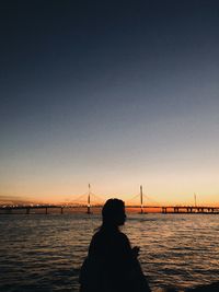 Rear view of silhouette person on suspension bridge against sky during sunset