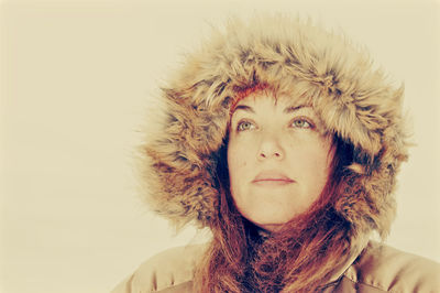 Close-up of thoughtful mature woman in warm clothing looking away against beige background