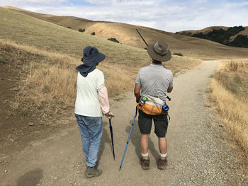 Rear view of hikers with hiking cane standing on road