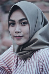 Close-up portrait of woman wearing hijab against brick wall