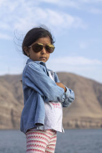 Girl wearing sunglasses while standing at beach against sky