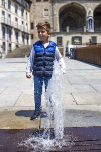Full length of boy standing by fountain in city