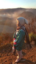 Side view of woman standing on mountain against sky during sunset