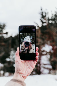 Cropped hand of woman holding smart phone while photographing outdoors during winter